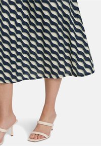 Jupe midi à motifs vagues navy et crème avec un design fluide ; associée à des sandales à talons à lanières beige clair.