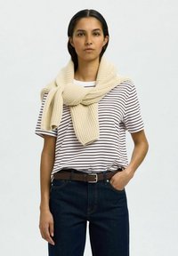 Strikket kremfarget skjerf lagt over en hvit og marinblå stripete T-skjorte, parret med mørkeblå jeans og et brunt belte. Enkel, ren design.