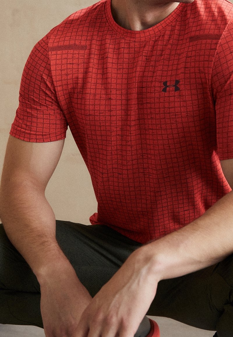 Camiseta atlética roja con un patrón de cuadrícula, hecha de una tela texturizada. Cuenta con un cuello redondo y un pequeño logo negro en el pecho.
