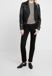 Svart läderbikerjacka över en blus med svart-vita mönster, tillsammans med svarta slim-fit jeans och svarta loafers.