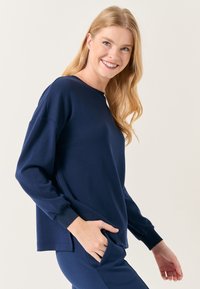 Felpa a maniche lunghe blu navy in tessuto morbido con collo rotondo, polsini a coste e una vestibilità rilassata. Tasca laterale visibile.