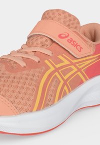 Παιδικό αθλητικό παπούτσι Asics σε ροδακινί και πορτοκαλί χρώμα με λουράκι με βέλκρο, κορδόνια μπροστά, ανθεκτικό διχτυωτό επάνω μέρος και λευκή μαξιλαρωμένη σόλα.