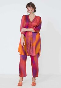 Felkleurige, lichte stoffen outfit bestaande uit een knoop-sluiting, langmouwige top met V-hals en bijpassende broek, in oranje, roze en paars.