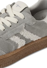 Baskets grises avec des détails en daim et en fourrure texturée blanche, lacets crème, semelle en caoutchouc et une étiquette de logo grise sur la languette.