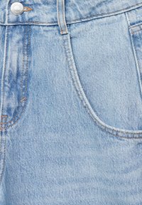 Poche de jean en denim bleu clair avec des coutures orange visibles et un bouton métallique à la taille.