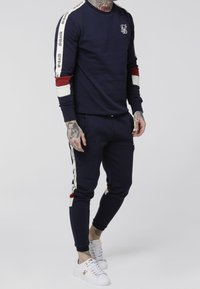 Sudadera azul marino y joggers a juego en una tela suave, con acentos a rayas en rojo, blanco y con marca en las mangas y los lados.