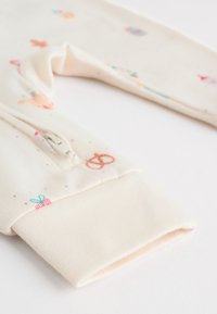 Sweat-shirt crème clair pour tout-petit avec motifs ludiques, fermeture éclair à l'avant et poignets côtelés, fabriqué en tissu doux pour plus de confort.
