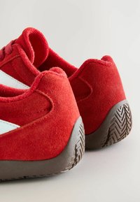 Red suede athletic shoes with a textured finish, featuring a white stripe on the side and a durable brown rubber outsole with a zigzag pattern.