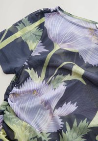 Lillelille lilledega top, millel on suured lillad lilled ja rohelised lehed tumedal taustal. Kerge, tekstuuriga kangas, millel on kokku volditud detail.