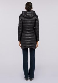 Svart puffjacka med horisontell quiltstruktur, figursydd design, huva och sidoflikar. Matchad med mörka jeans och svarta skor.