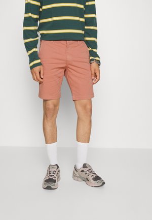 Shorts rose clair avec ourlets roulés, assortis à un haut à manches longues rayé vert et jaune, chaussettes blanches et baskets grises.