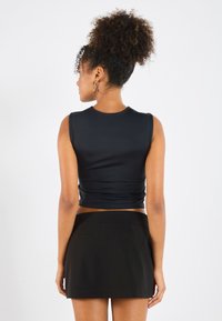 Black sleeveless crop top made of smooth fabric with a fitted design. Paired with a high-waisted, short black skirt featuring back pockets.