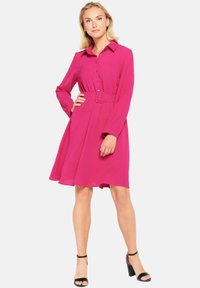 Fuksia mekko kauluksella, napit edessä, pitkät hihat, vyötäröllä vyö ja levenevä hame. Yhdistetty mustiin korkokenkiin.