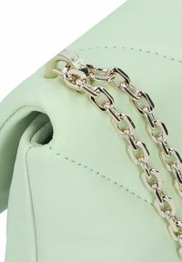 Borsa a mano in pelle verde chiaro con finitura testurizzata, dotata di una tracolla in catena dorata e dettagli cuciti. Forma arrotondata con design a piega.