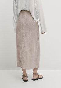Jupe maxi en lin beige avec une coupe droite, surface texturée, taille haute, portée avec des sandales noires. La vue arrière met en avant la simplicité du design.