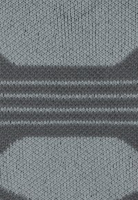 Primo piano di un tessuto lavorato a maglia con grandi ovali grigi e strisce scure su uno sfondo grigio chiaro.