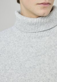 Pull à col roulé côtelé gris clair en tissu doux, avec un col haut et un motif texturé. Vue en gros plan de l'encolure.