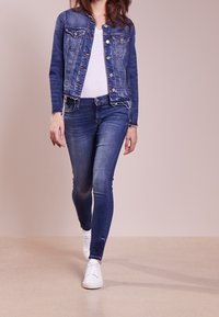 Jeanstjacka i mörk tvätt, med metallknappar och två bröstfickor, ihop med ljusblå skinny jeans och vita sneakers.