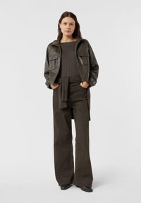 Brązowa skórzana kurtka z dwoma przednimi kieszeniami, zestawiona z ciemnobrązową bluzką i spodniami z wysokim stanem o szerokich nogawkach. Całość uzupełniają czarne buty.