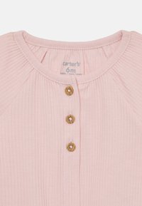 Lichtroze geribbelde babytop met een ronde halslijn, voorzien van drie houten knopen en een verzorgingslabel met de tekst "carter's, 6m" aan de binnenkant van de nek.