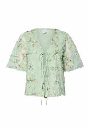 Blusa verde chiaro con ricami floreali in blu, scollo a v, nodo frontale e maniche corte, realizzata in un tessuto morbido e testurizzato.