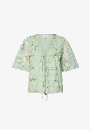 Blusa verde chiaro con ricami floreali in blu, scollo a v, nodo frontale e maniche corte, realizzata in un tessuto morbido e testurizzato.