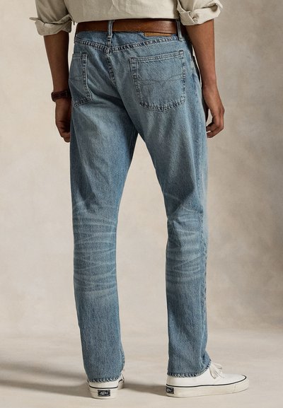 Calças de ganga azul claro com corte de perna reta, costuras visíveis, cinco bolsos e textura desgastada, combinadas com ténis brancos.