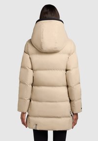 Woman wearing a beige quilted puffer coat with a large hood, shown from the back against a plain gray background.