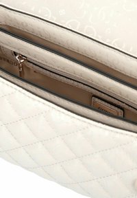 Sac à main matelassé blanc avec plusieurs compartiments, y compris une poche zippée et un intérieur en tissu beige avec une petite étiquette métallique de la marque.