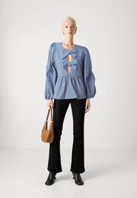 Ριγωτή μπλε μπλούζα με φουσκωτά μανίκια, κοψίματα σε σχήμα κλειδώματος και δύο φιόγκους. Συνδυασμένη με μαύρες καμπάνα παντελόνες και καφέ τσάντα.