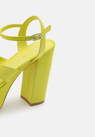 Talons hauts en suède jaune avec un large talon bloc et une sangle de cheville réglable. Dotés d'une doublure intérieure lisse et d'un design à bout rond.