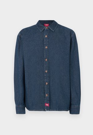 Sötétkék farmer gombos ing hegyes gallérral, hosszú ujjakkal és rézszínű gombokkal. A bal oldalon egy kis piros címke található.