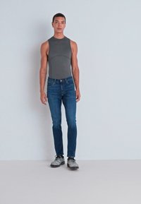 Grå ermeløs body, blå tettsittende jeans og grå sko. Glatt tekstur, figursydd design og lett sømdetalj på jeans.