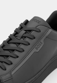 Baskets en cuir noir avec des lacets plats texturés. Présentent un logo distinct 'BOSS' et un design élégant. Semelle en caoutchouc avec des détails minimalistes.