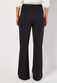 Pantaloni neri a palazzo con una texture liscia, passanti per cintura e due tasche posteriori. Il tessuto appare leggero e sartoriale.