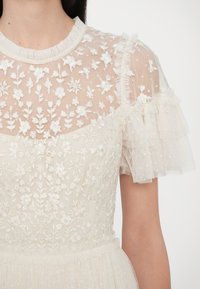 Beiges Kleid mit durchscheinendem, besticktem Oberteil, das florale Muster aufweist, sowie kurzen, gerafften Tüllärmeln und einem strukturierten Rock.