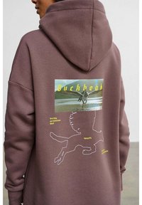 Hnědá mikina s kapucí s velkým grafikou koně na zádech, žlutým textem a bílým obrysem běžícího koně. Měkká, texturovaná látka.