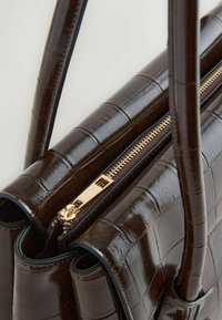 Brown crocodile-embossed leather handbag with gold-tone zipper, dual handles, and structured shape. Features textured surface and stitching details.