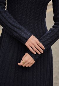 Marineblå kabelstrikket kjole med lange ærmer og en tætsiddende silhuet. To ringe pryder hænderne og supplerer det teksturerede stof.