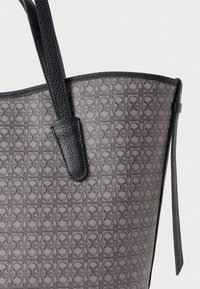 Bolsa de mão feita de material cinza texturizado com detalhes em couro preto. Apresenta um design padrão e duas alças resistentes.