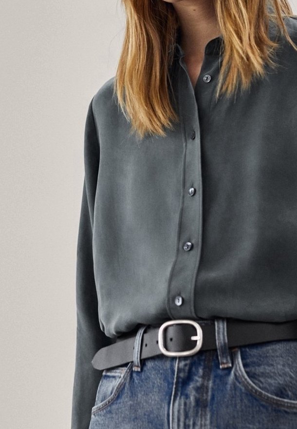 Personne portant une chemise gris foncé boutonnée rentrée dans un jean bleu avec une ceinture noire avec une boucle argentée.