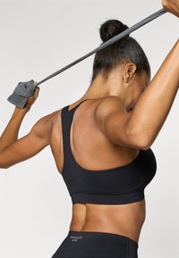 Μαύρο αθλητικό σουτιέν με σχέδιο racerback, λεία υφή και φαρδιές ράντες στους ώμους. Ξεχωρίζει για το μινιμαλιστικό στυλ και το έντονο χρώμα του.