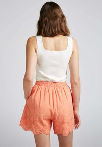 Débardeur blanc à côtes avec un décolleté carré, associé à un short corail présentant des motifs floraux brodés et un ourlet en dents de scie.