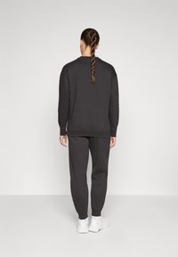 Mörkgrå sweatshirt och matchande joggers med ribbade manschetter. Tyget verkar mjukt och har en avslappnad passform. Kombinerat med vita sportskor.
