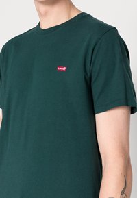 Tmavě zelené bavlněné tričko s krátkým rukávem a kulatým výstřihem, na levé části hrudi s malou červenou nášivkou loga Levi's.