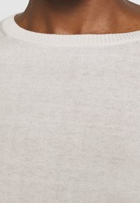 Lichtbeige gebreide trui met een ronde halslijn en een ribbelstructuur. Het materiaal lijkt zacht, met een subtiel, fijn gebreid patroon.