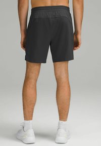 Svarta idrottsshorts med elastiskt midjeband, sidofickor och ett mjukt, lätt tyg. Modellen bär vita sneakers.