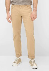 Beige chino's met een slim fit, gemaakt van zacht katoen, voorzien van vijf zakken, riemlussen en omgeslagen pijpen, gecombineerd met beige sneakers.