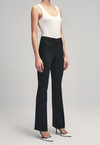 Pantalon noir évasé en tissu lisse, assorti à un débardeur blanc côtelé et des talons pointus noirs et blancs. Design simple avec une taille ajustée.