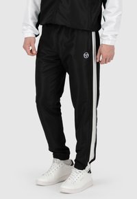Zwarte trainingsbroek van glad materiaal, met witte zijkanten en een klein logo. Elastische enkels met een relaxte pasvorm.